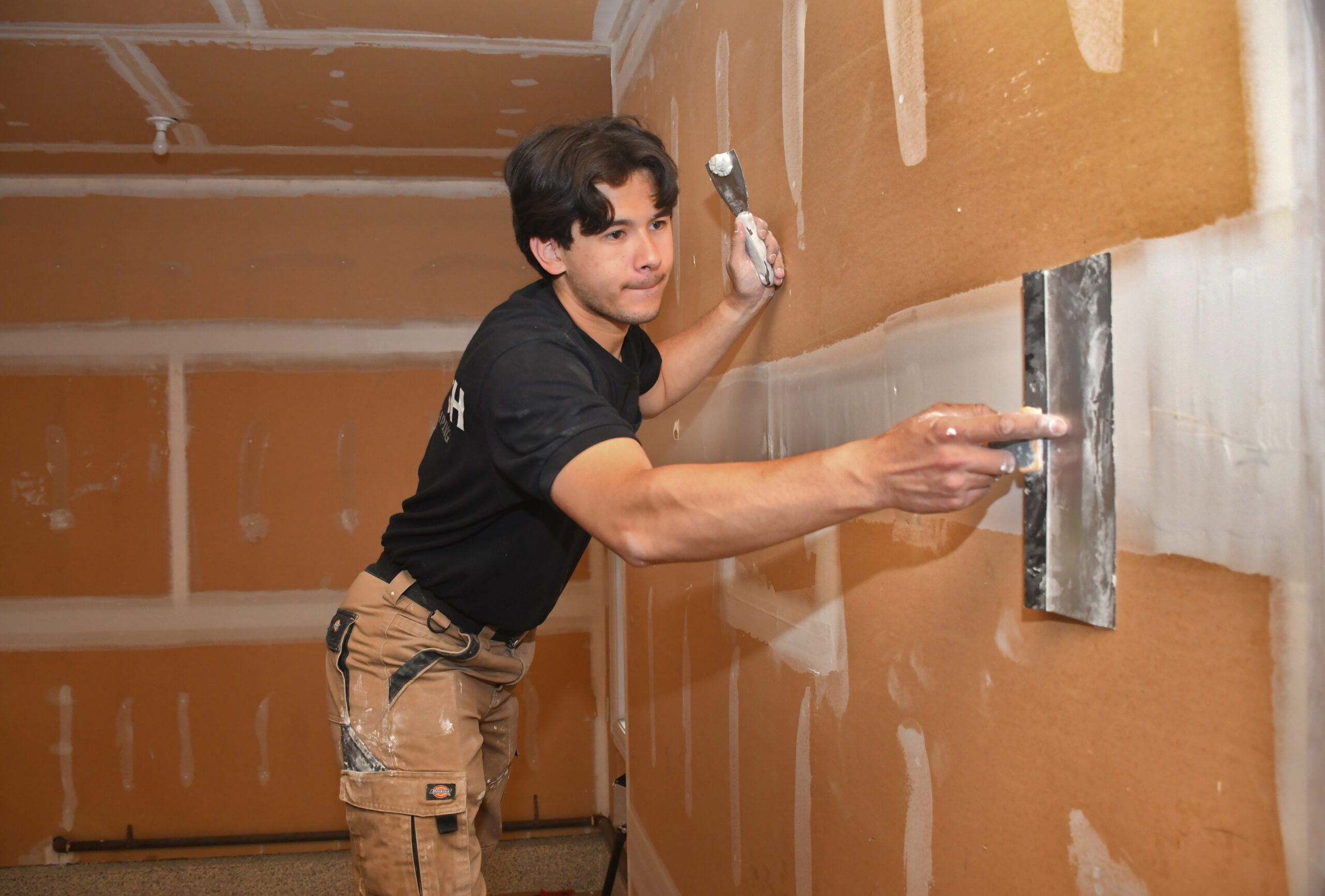 Construction worker smoothing plaster onto a brown wall with a trowel inside a room under renovation